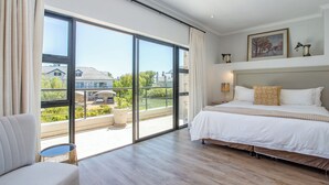 A bedroom with a large sliding glass door to a balcony, a bed with white bedding, a small round table, and a chair. - Valley Golf Lodges (Paarl)