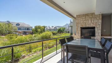 A modern outdoor dining area with a stone fireplace, a glass table, and chairs.
