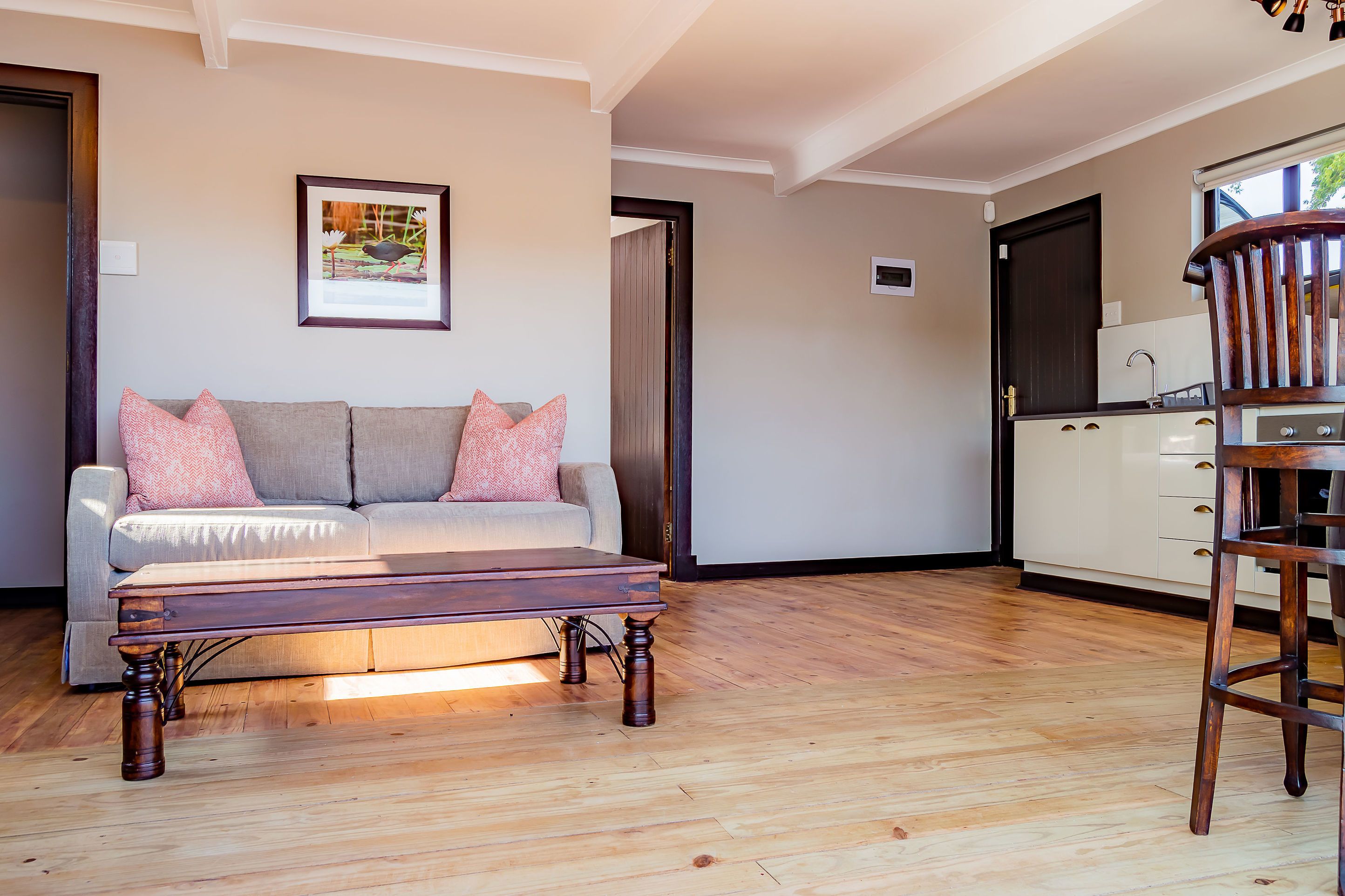 A living room with a sofa, a wooden coffee table, and a kitchen area with cabinets and a chair.