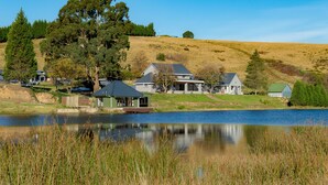 A lakeside property with multiple houses, a dock, and a grassy hill in the background.