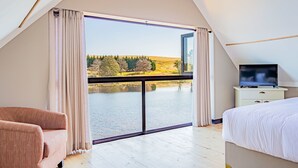 A bedroom with a large sliding glass door leading to a lake view, a bed, a TV on a bedside table, and a chair.