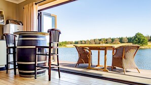 A wooden deck with a table and chairs, a large barrel, and a view of a lake and trees.