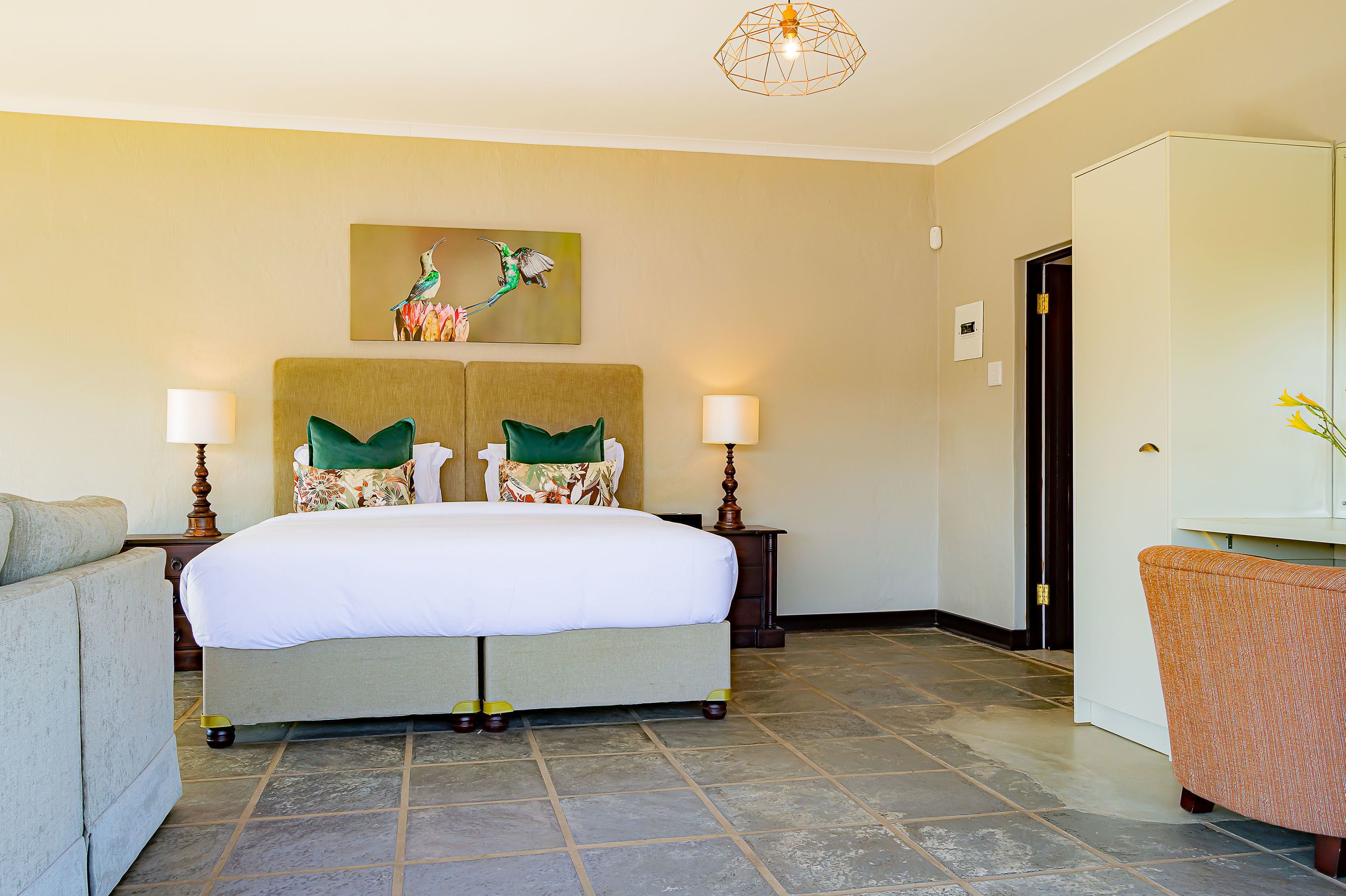 A hotel room with a large bed, two bedside tables with lamps, a sofa, and a painting of a hummingbird on the wall.
