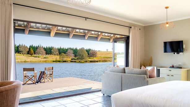 A bedroom with a large window, a bed, a sofa, and a desk with a TV.