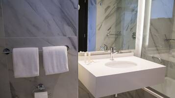 Un baño moderno con pared de mármol, cabina de ducha de vidrio y lavamanos blanco.