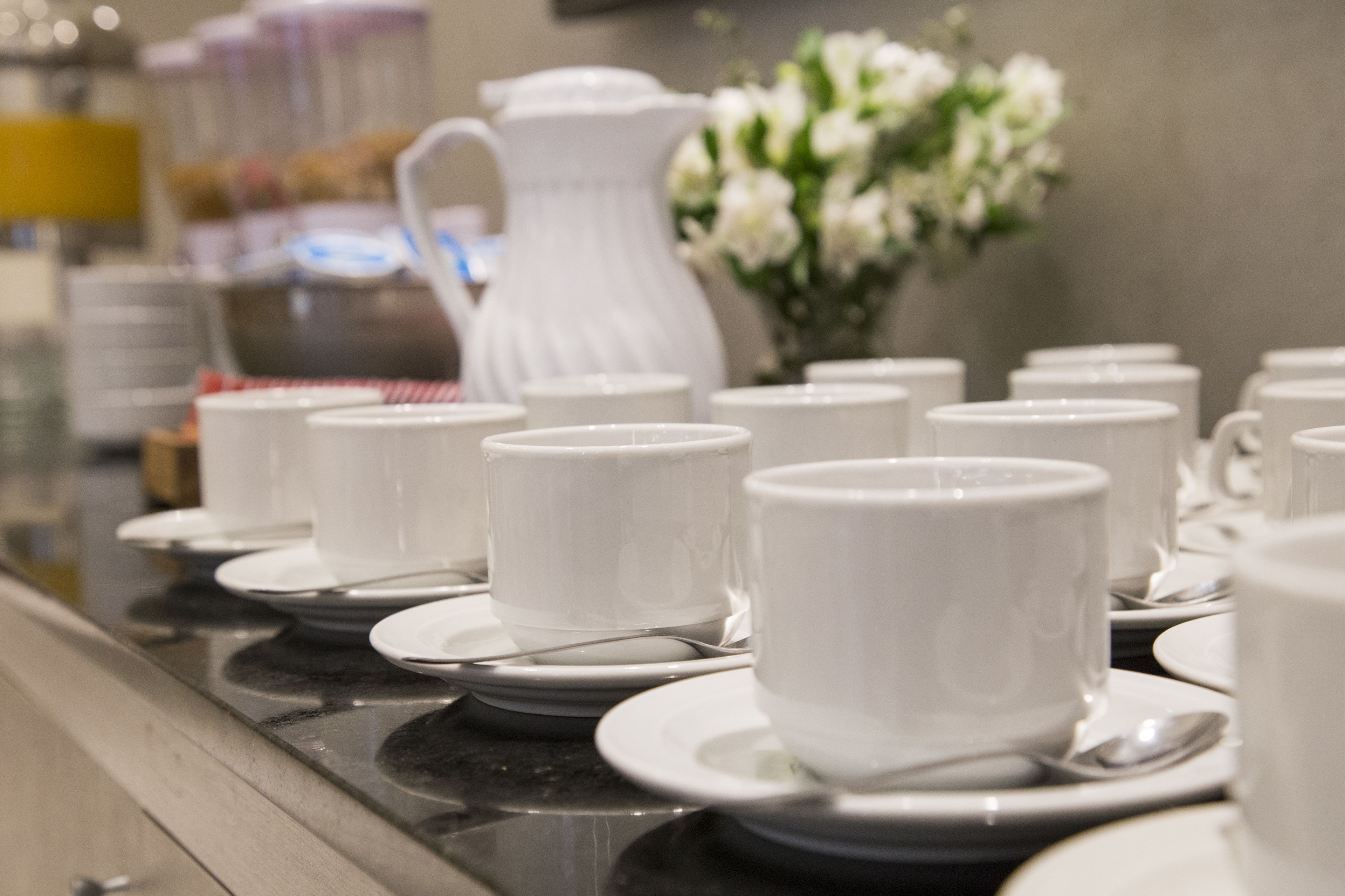 Dispositiu de buffet amb tasses i platets blancs, una gerra blanca i un arranjament floral.