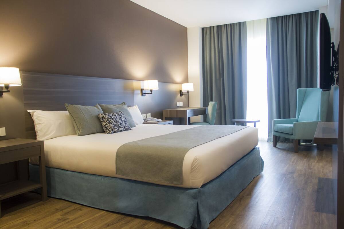Een hotelkamer met een groot bed, nachtkastjes, een bureau, een stoel en een televisie.