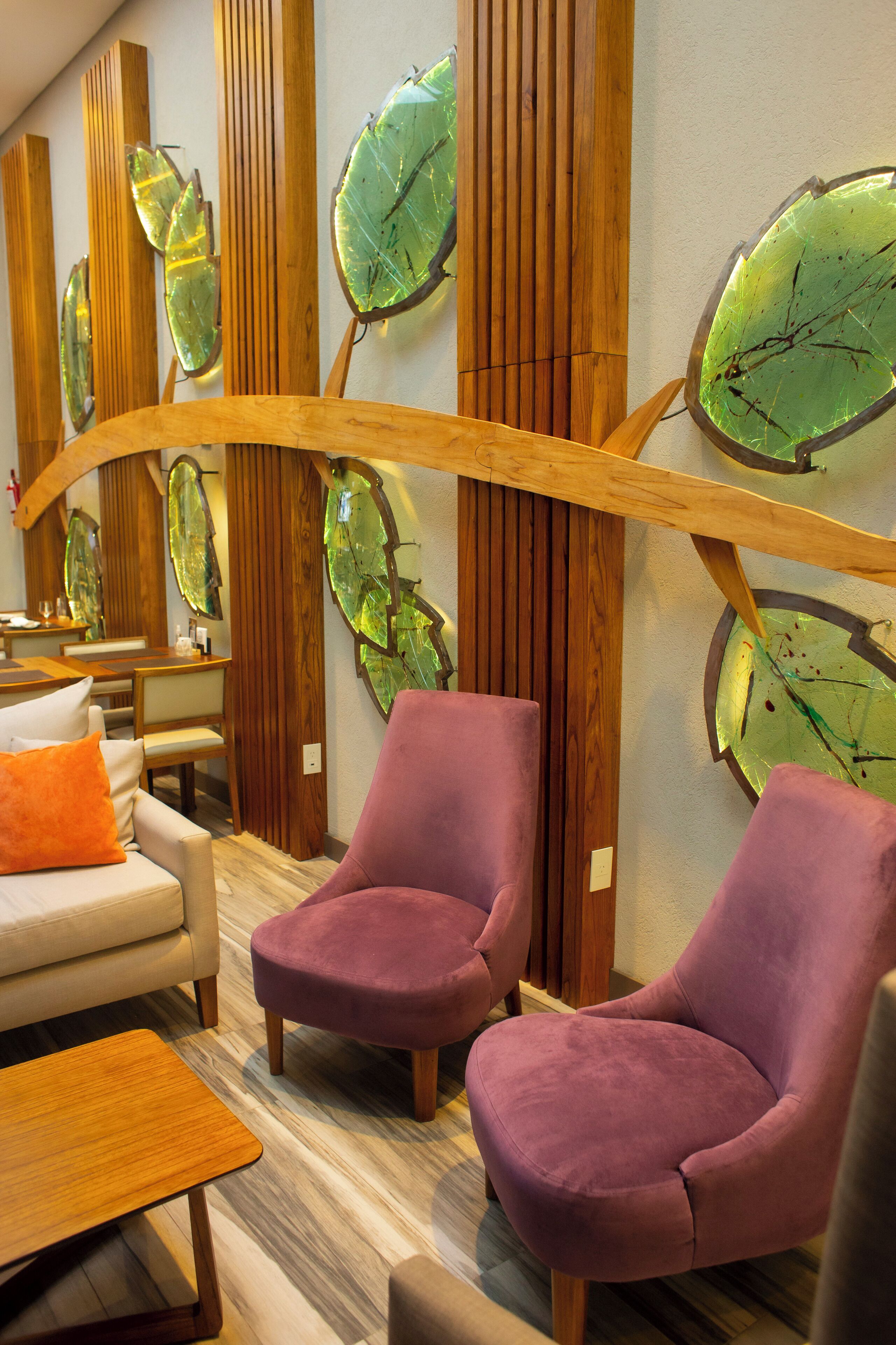 Ein modernes Interieur mit Holzwandverkleidung, einem Sofa mit orangefarbenem Kissen und zwei violetten Sessel.
