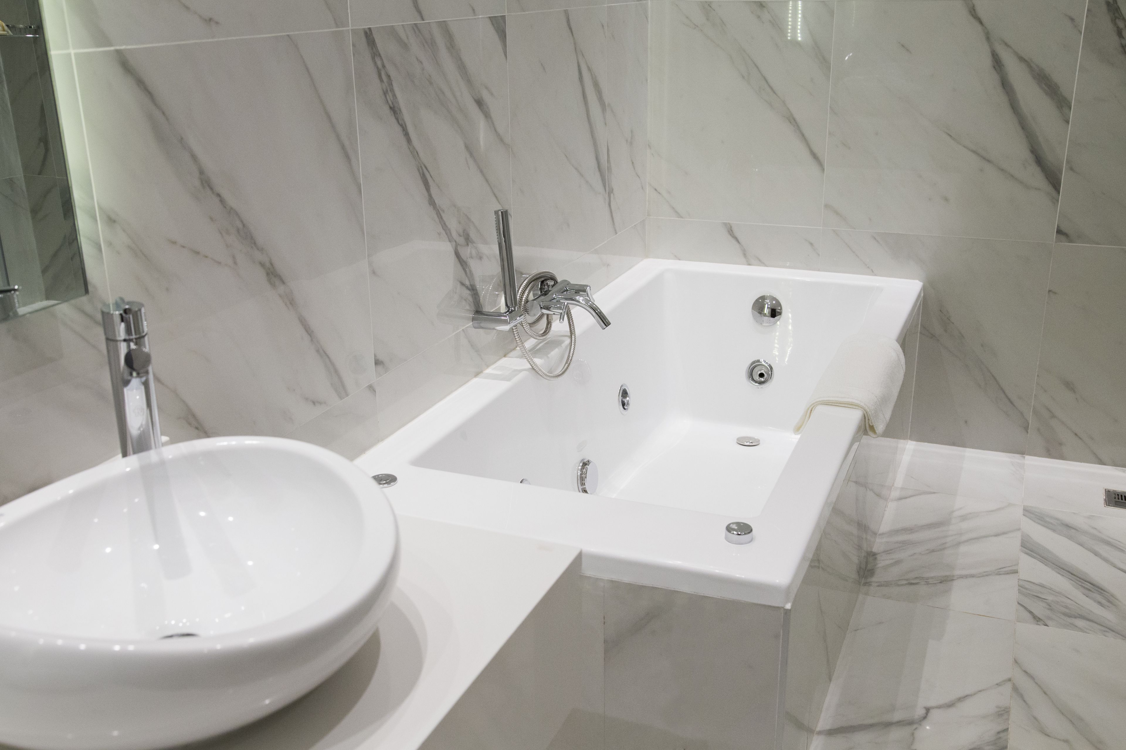 A modern bathroom with a white bathtub, a round sink, and marble walls.
