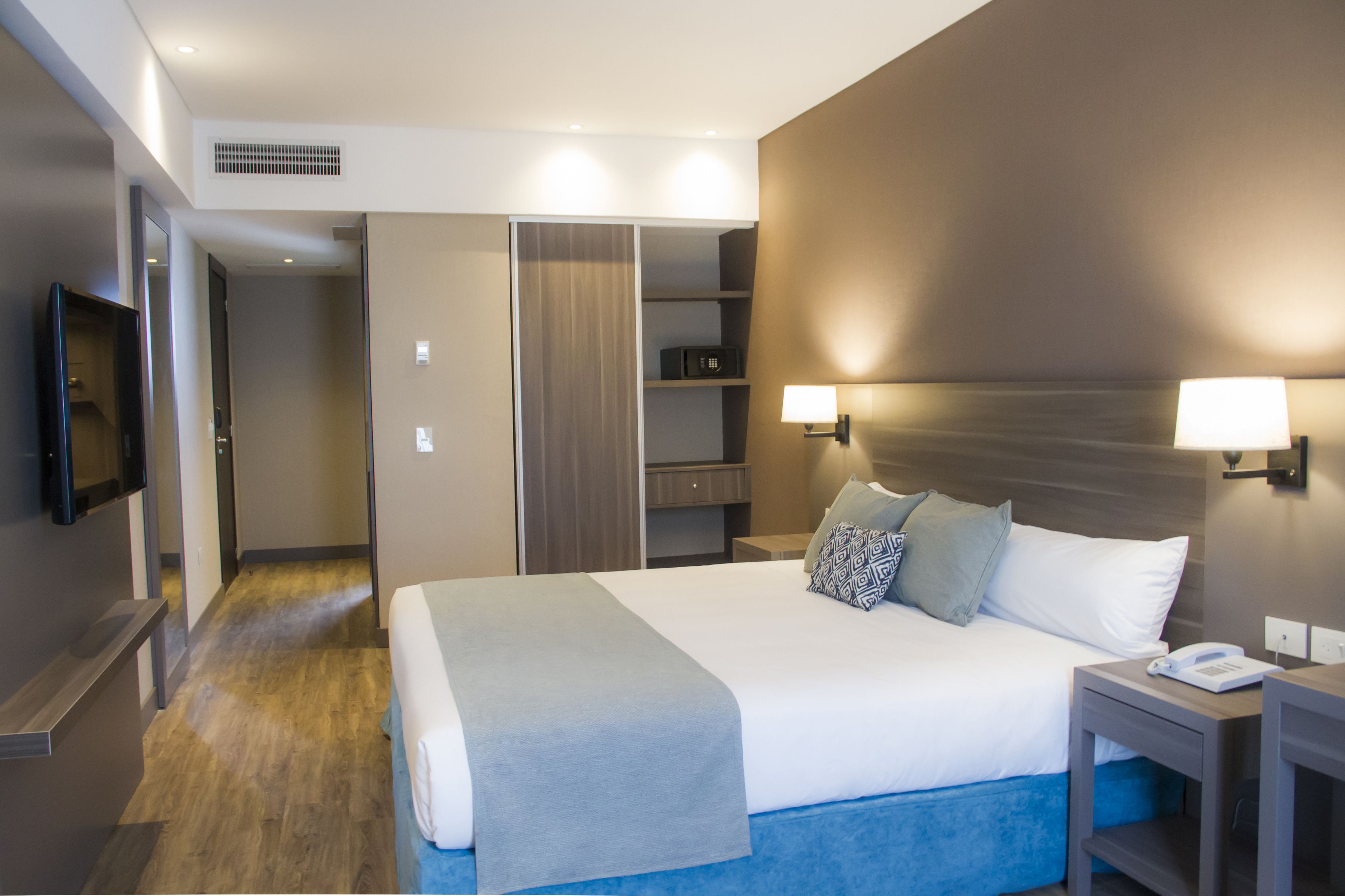 A modern hotel room with a large bed, bedside lamps, a TV, and a walk-in closet.