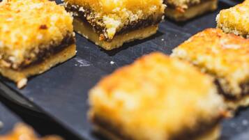 Une assiette contenant des desserts carrés à la croûte dorée, peut-être un type de gâteau ou de pâtisserie, posée sur une surface sombre en ardoise.