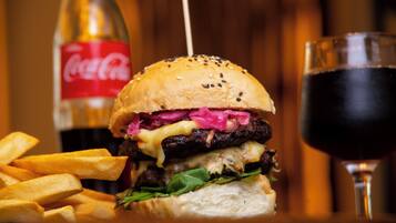 Una hamburguesa con papas fritas y un vaso de bebida oscura, posiblemente Coca-Cola, sobre una mesa de madera.