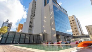 Ein modernes Gebäude mit einer reflektierenden Glasfassade, einem Swimmingpool mit Liegestühlen und einem Holzdeck.