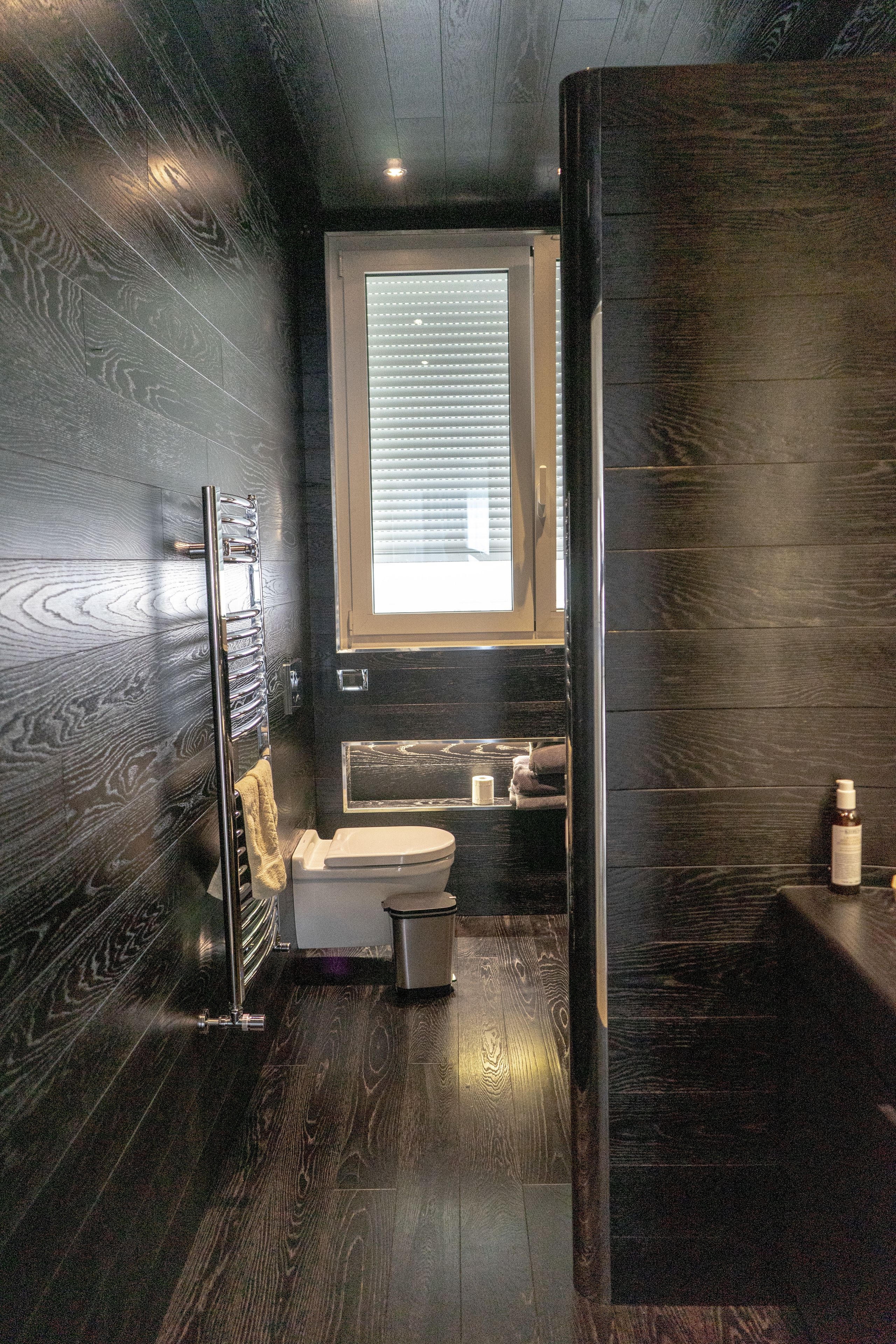 Ein modernes Badezimmer mit dunklem Holzboden, einer Duschkabine aus Glas und einem WC mit Handtuchhalter.