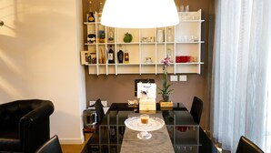 A dining area with a glass table, black chairs, a white pendant light, and a shelf with various items. - Apartments Residence Villa Olmo (Como)