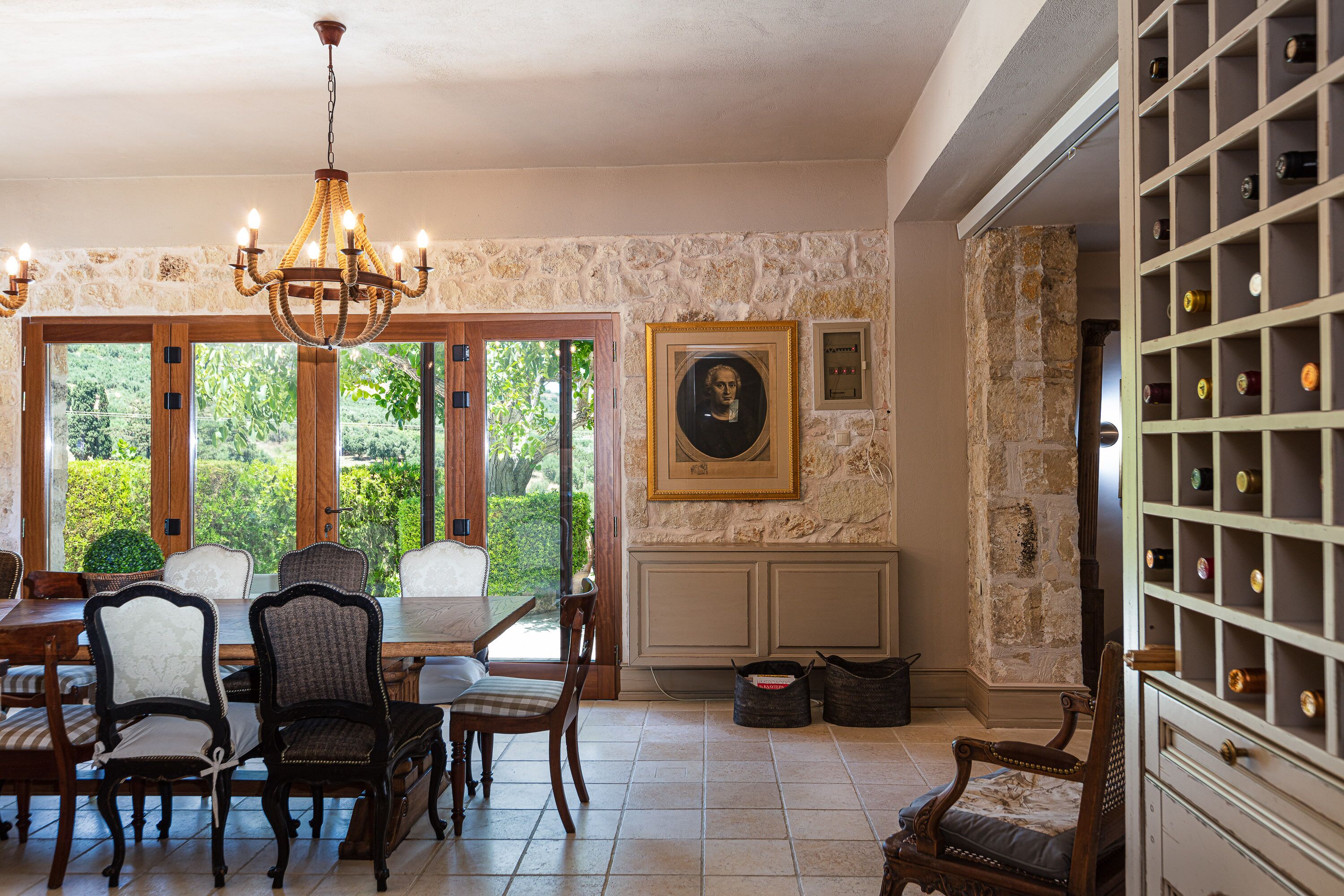 Un comedor con candelabro, pared de piedra, obras de arte enmarcadas y una estantería para vinos.