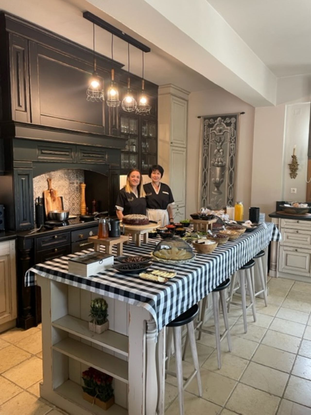 Una cocina con armarios oscuros, una isla central con mantel a cuadros y lámparas colgantes.