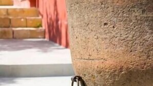 A large stone urn with a metal ring, positioned in front of a red building with barred windows and a staircase. - Nicuzza House with panoramic infinity pool (Avola)