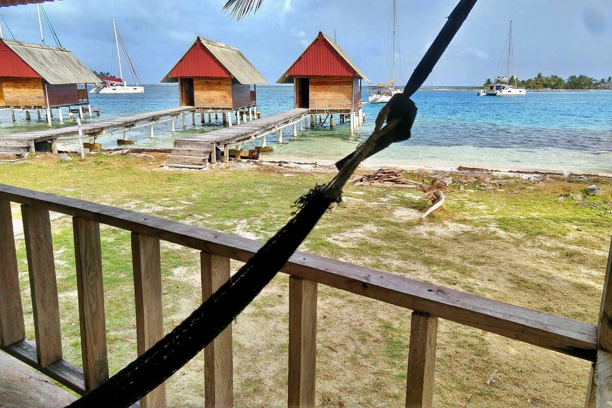 A wooden deck with a hammock, a pier with overwater bungalows, and boats on the water.