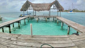A wooden pier leading to a thatched-roof structure over a clear blue pool. - Private wood Cabins on San Blas island - private bathroom (Narganá)
