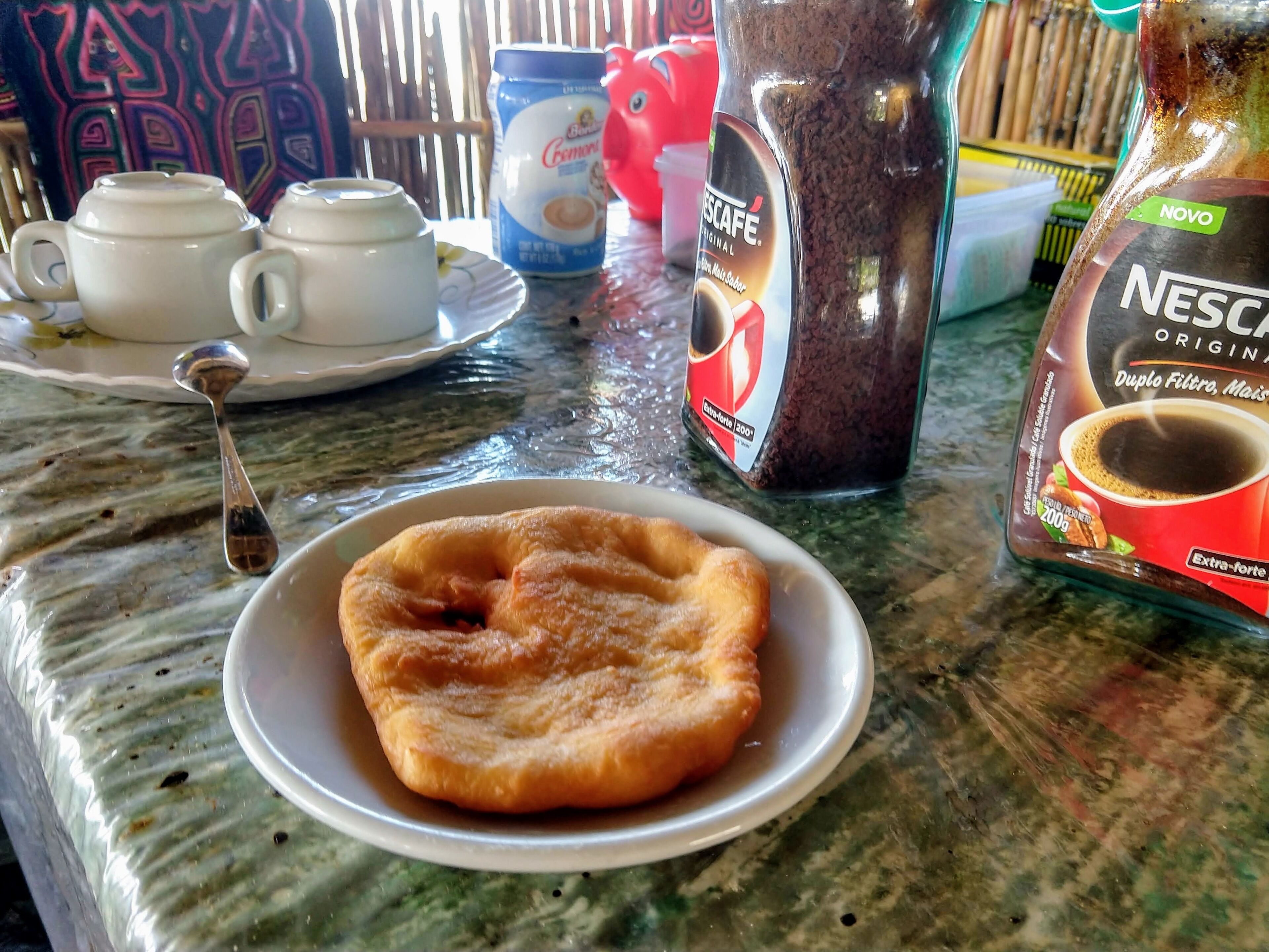 Disposição para o café da manhã com um prato de doces, uma cafeteira e um sachê de café Nescafé.