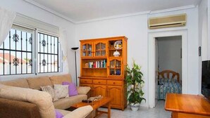 A living room with a sofa, a wooden cabinet, a television, and a window with bars.