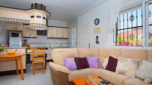 A compact living space with a kitchenette, a sofa, a dining table, and a window with decorative bars.