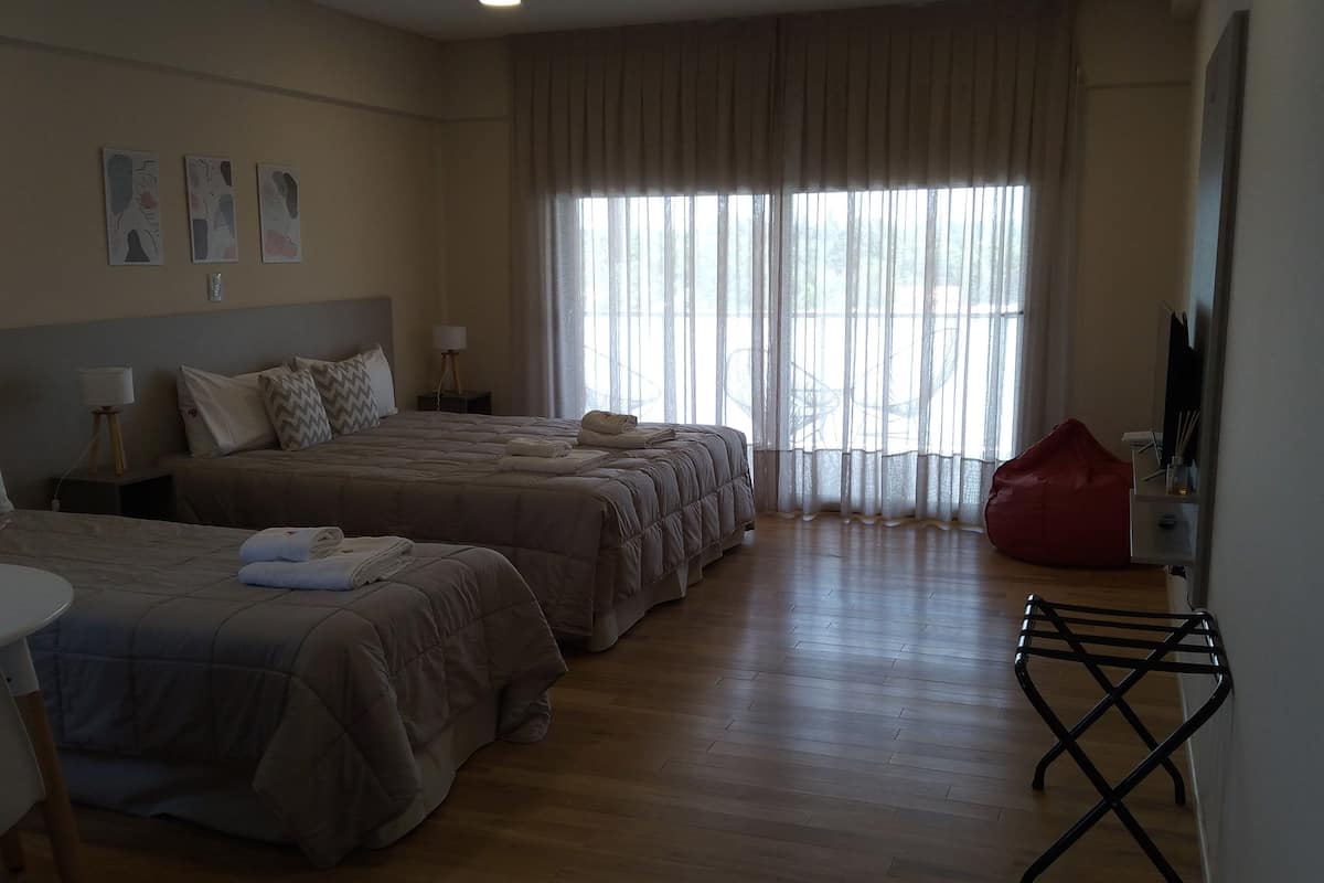 Une chambre d’hôtel avec deux lits, un bureau, une chaise, un pouf rouge et une télévision.