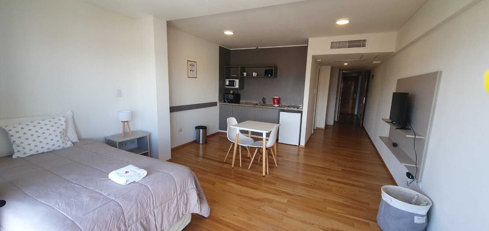 A hotel room with a bed, a desk, a chair, a microwave, a TV, and a small kitchenette.