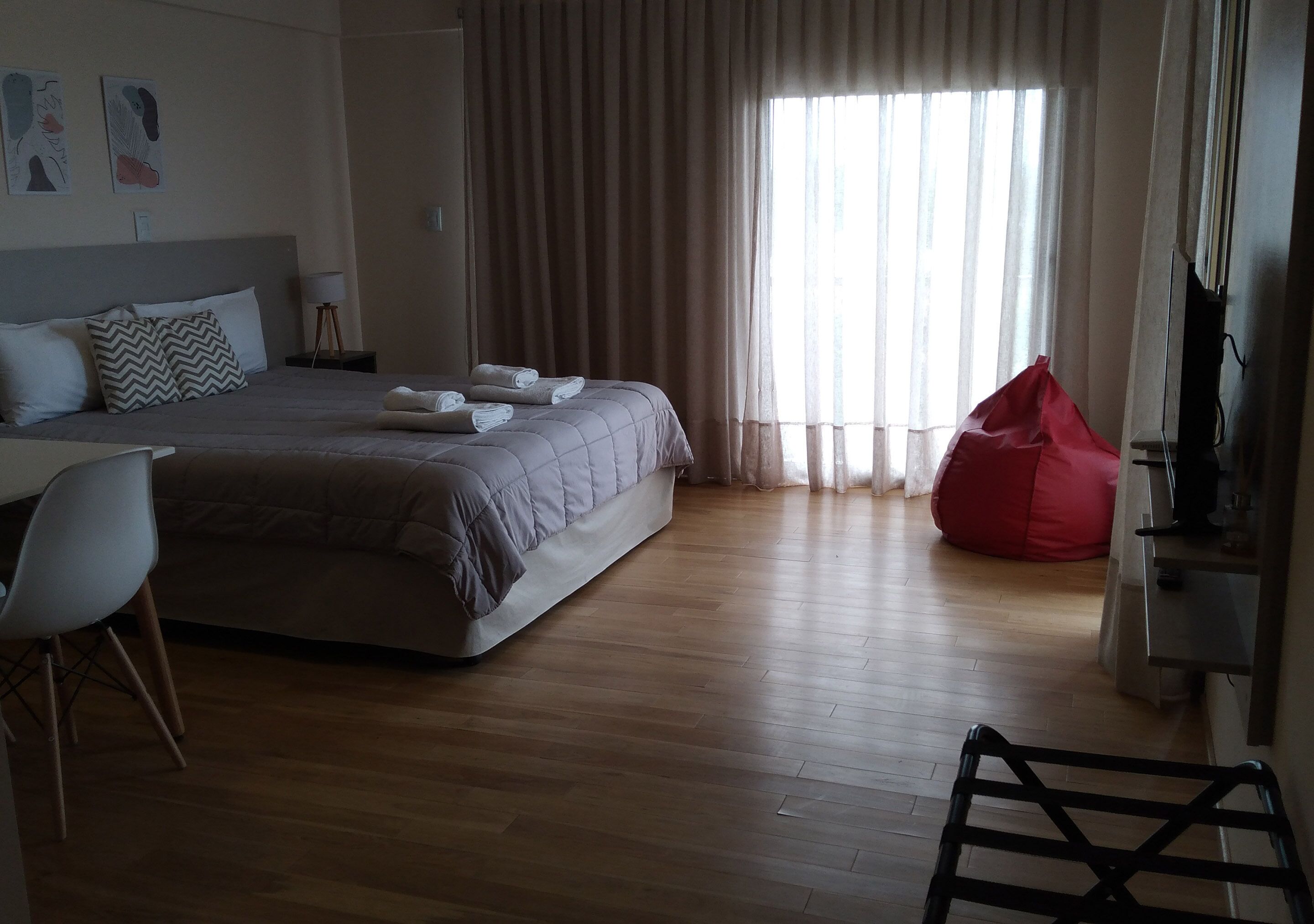 A hotel room with a bed, a desk, a chair, a red bean bag, and a television.