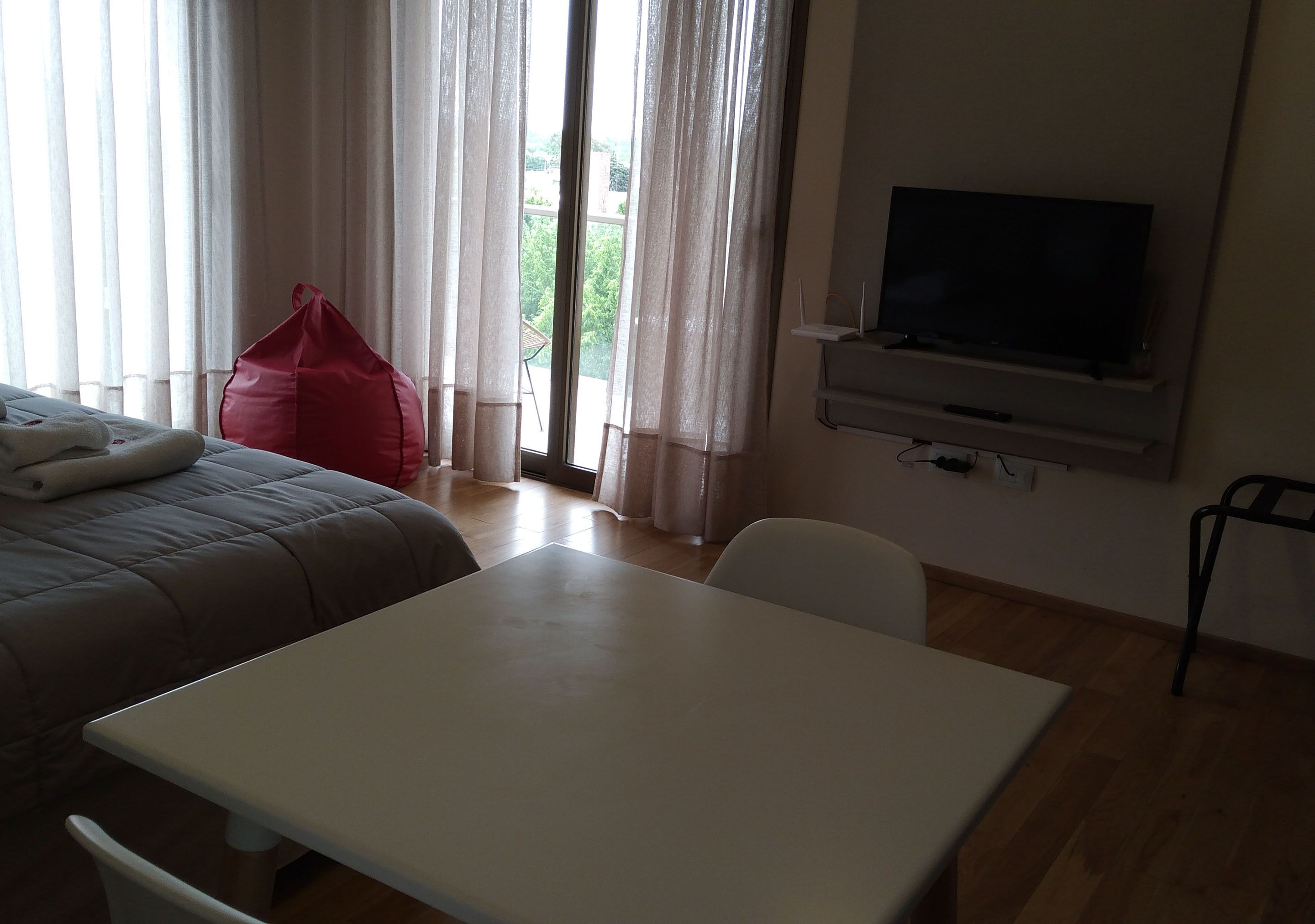 A hotel room with a bed, a table, a TV, and a window with curtains.