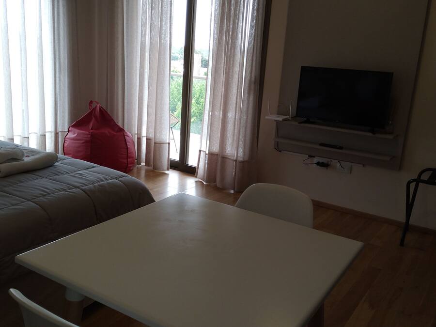 A hotel room with a bed, a table, a TV, and a window with curtains.