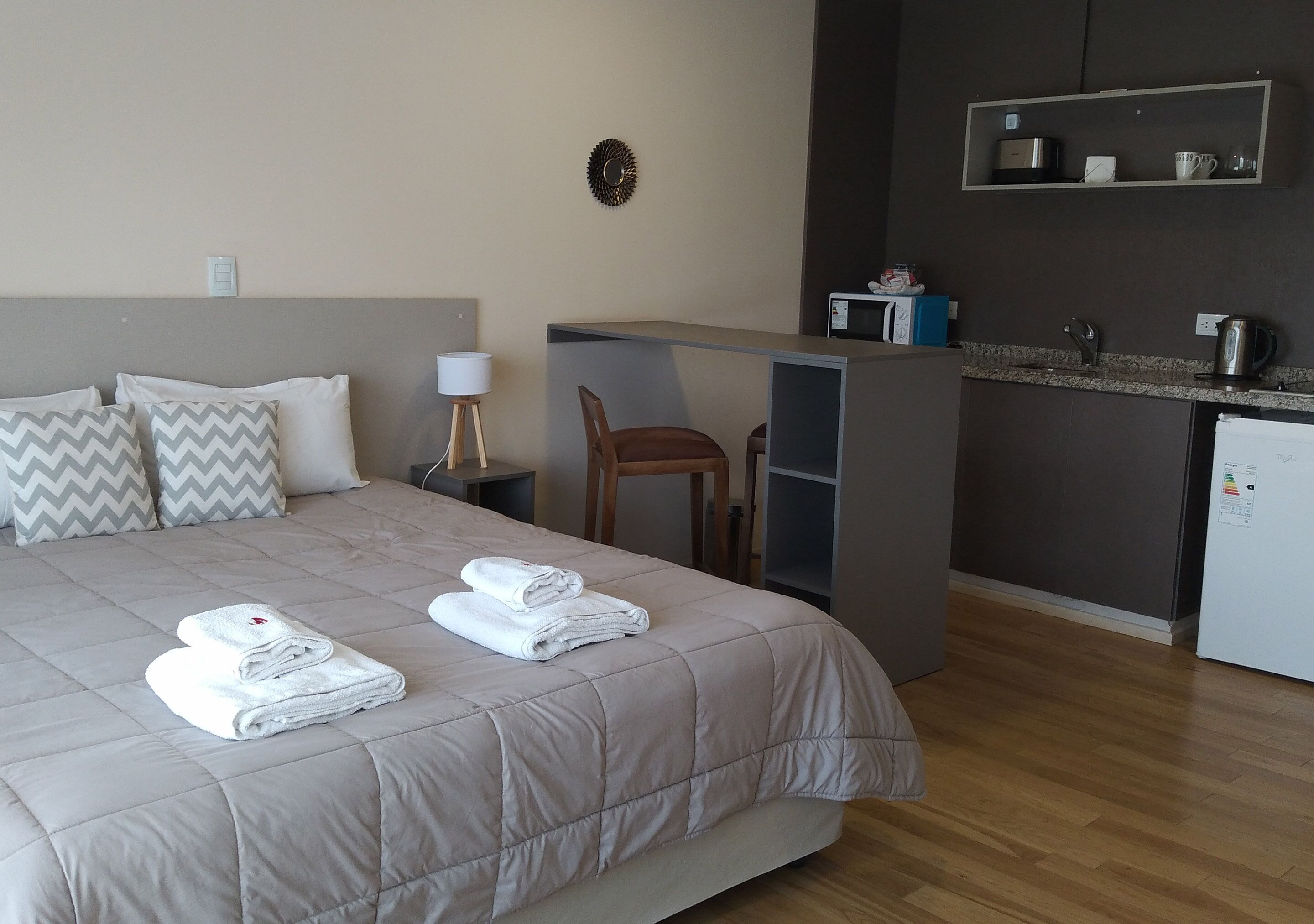 Een hotelkamer met een bed, een bureau, een stoel, een magnetron, een waterkoker en een kleine koelkast.
