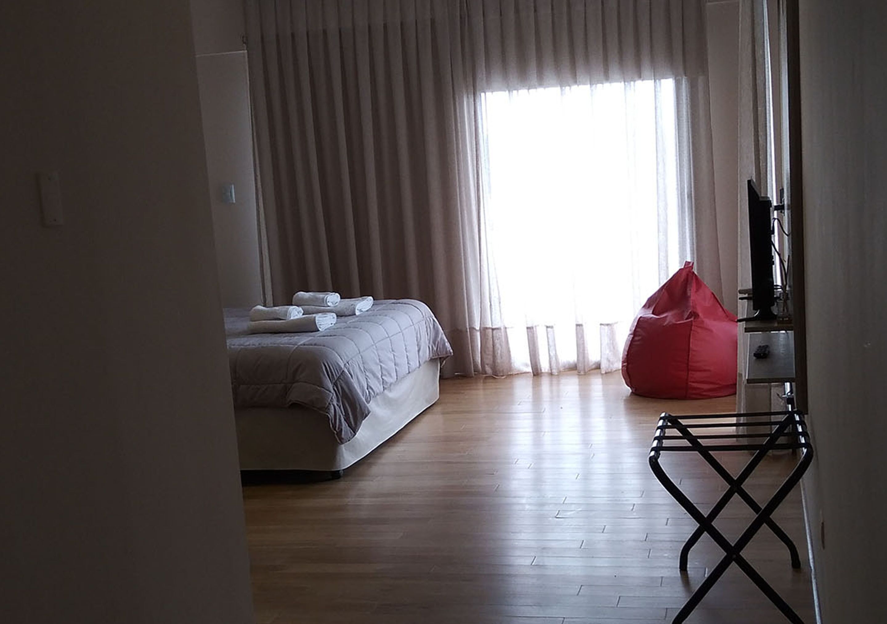 Un dormitorio con una cama, un sillón de mimbre rojo y un mueble para televisión.