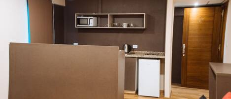 A compact hotel room with a kitchenette, a small refrigerator, and a wooden door.