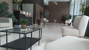 Un hall d’entrée moderne avec une table basse en verre, des fauteuils beiges et des plantes en pot.