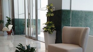 Un hall d’entrée moderne avec un fauteuil beige, une plante en pot et une cloison en verre.
