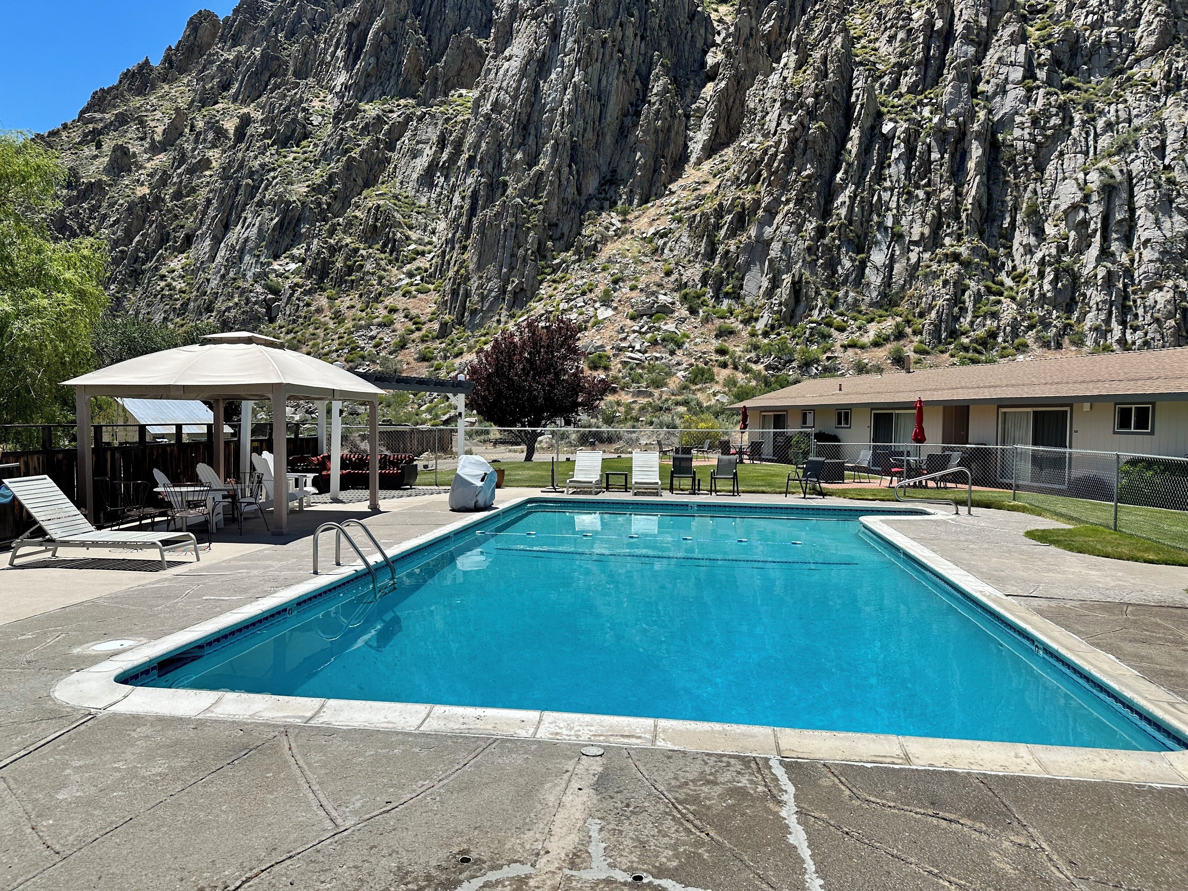A swimming pool with lounge chairs and a gazebo, surrounded by a mountainous landscape.