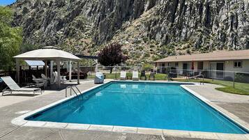 A swimming pool with lounge chairs and a gazebo, surrounded by a mountainous landscape.