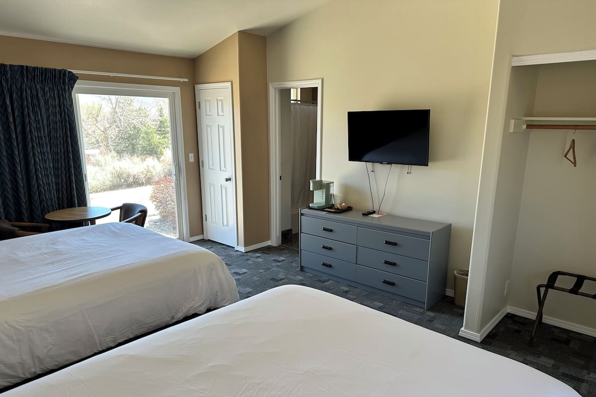 A hotel room with two beds, a TV, a dresser, a coffee maker, and a view of the outdoors.