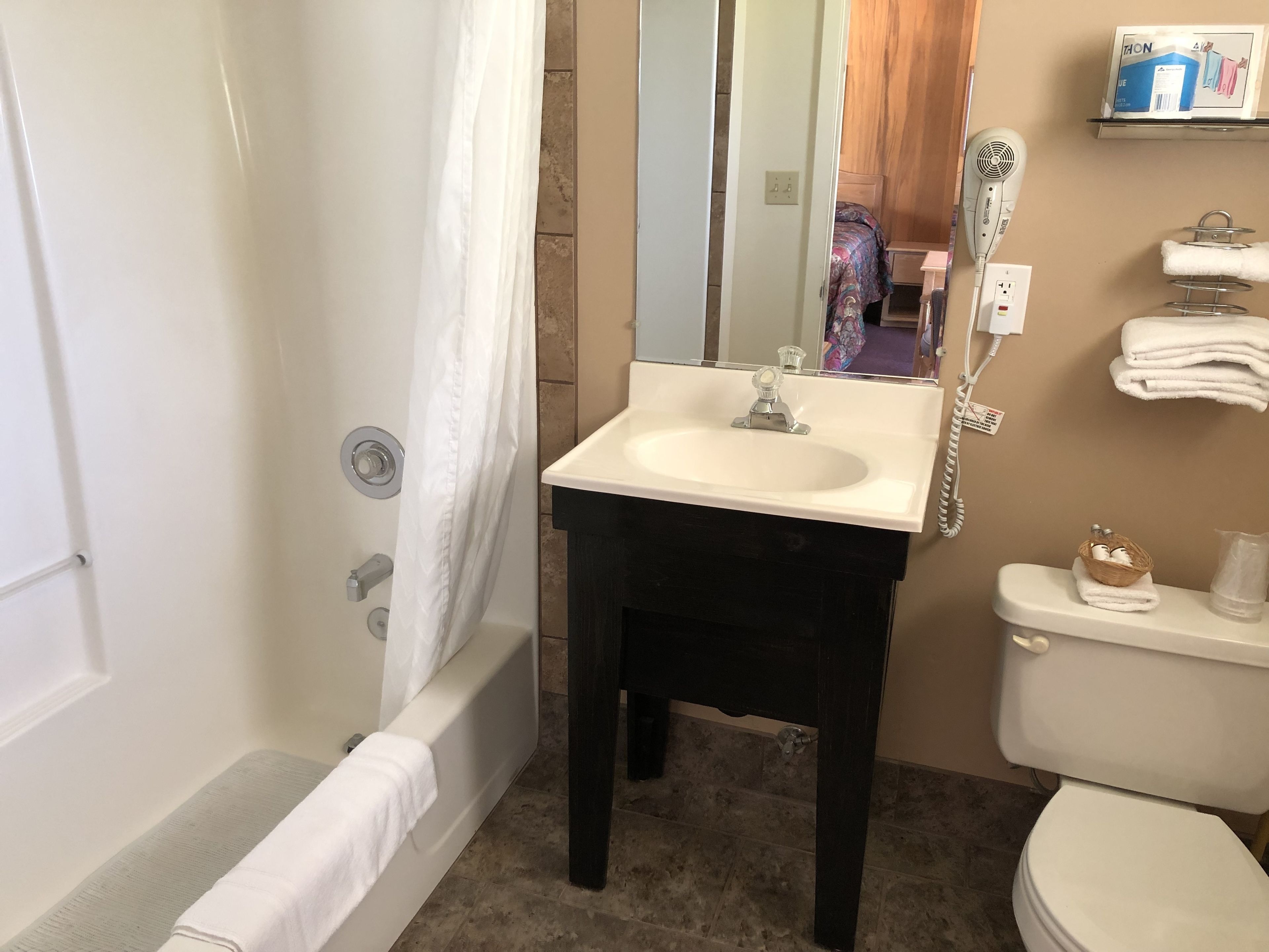 A bathroom with a white bathtub, a white sink with a mirror above it, a toilet, and a towel rack with towels.