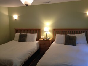 Two twin beds with wooden headboards, a bedside table with a lamp, and a wall-mounted light fixture. - Highland Dell Lodge (Monte Rio)