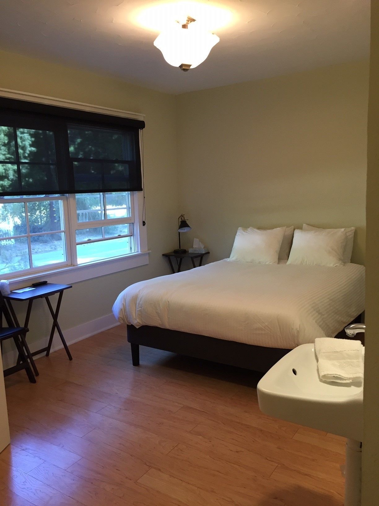 A bedroom with a bed, bedside table, lamp, and a window with blinds.