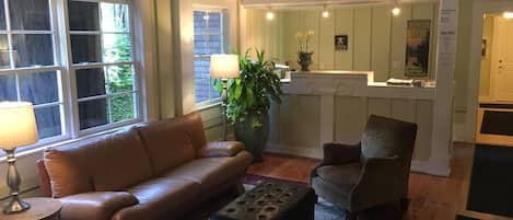 Ein Wohnzimmer mit Ledersofa, einem Sessel und einem Couchtisch. Ein großes Fenster, eine Pflanze und eine dekorative Wandverkleidung sind ebenfalls vorhanden.