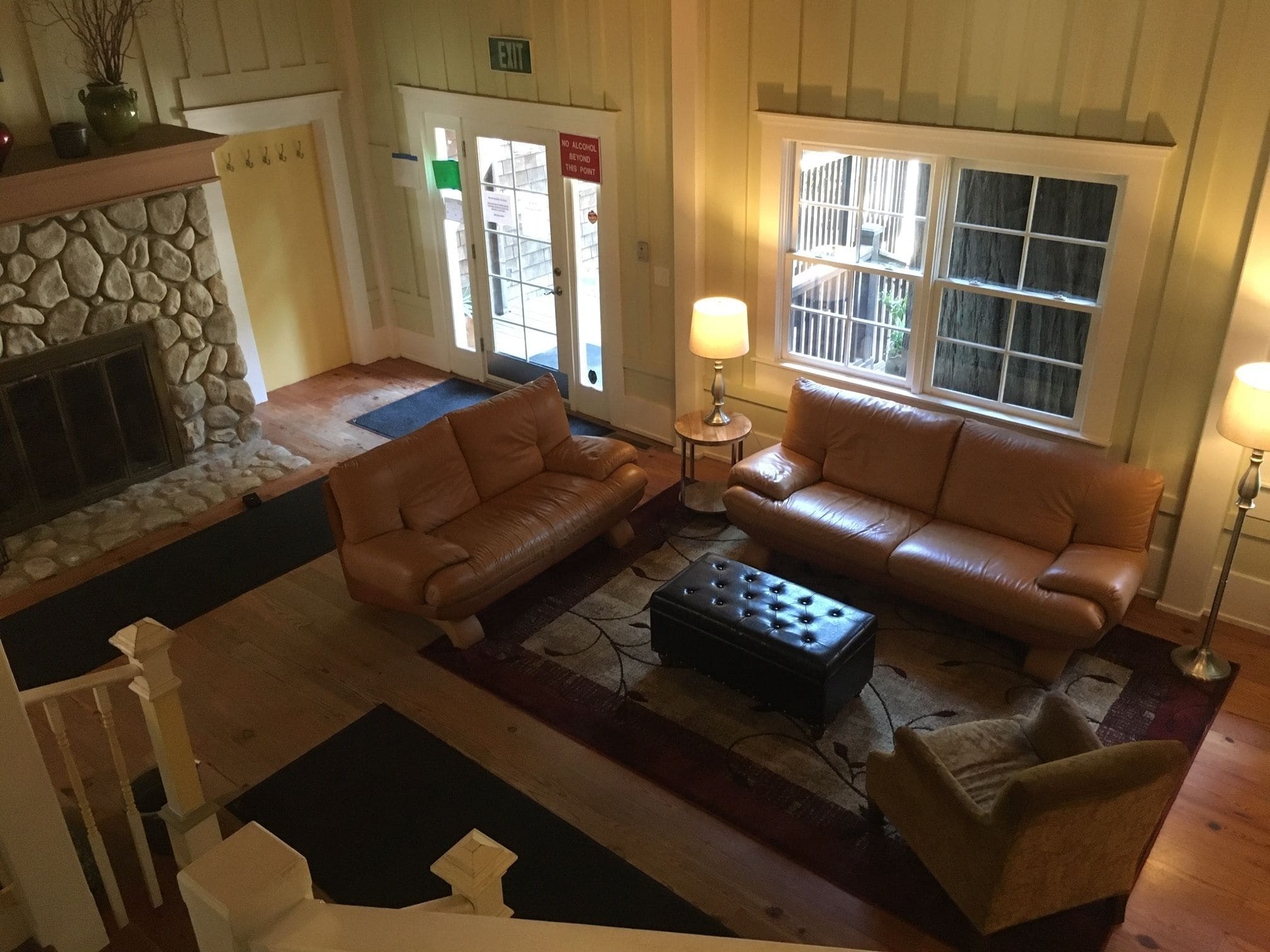 A living room with two leather sofas, a coffee table, and a stone fireplace. There is a door with an exit sign and a 'No Alcohol Beyond This Point' sign.
