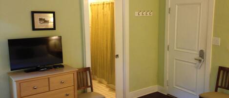 Una camera d'albergo con un letto, una televisione su un comodino, una sedia e una porta.