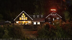 Un hôtel avec une enseigne « HÔTEL » bien visible, une grande vitrine illuminée et son reflet dans l’eau.
