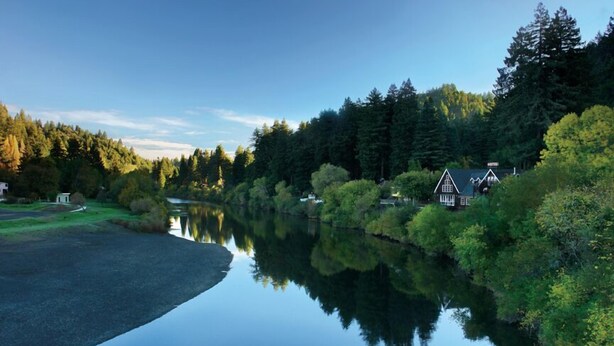 Une scène paisible au bord de la rivière, avec un hôtel et un petit bâtiment situés près de l’eau.
