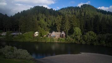 A lakeside lodge with a large house and a smaller cabin, surrounded by dense forest and a calm lake.