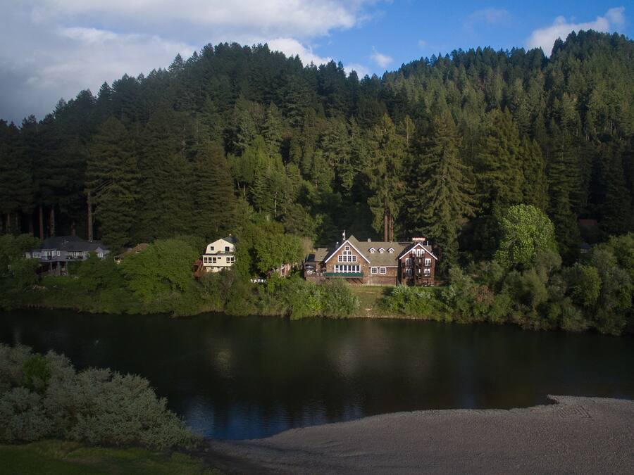 A lakeside lodge with a large house and a smaller cabin, surrounded by dense forest and a calm lake.